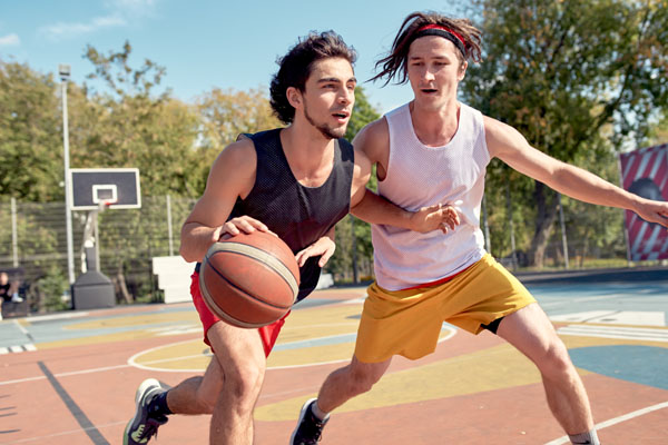 Picture of young sports men playing basketball on playground on summer day against background of green trees