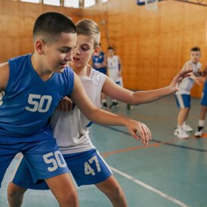 A junior basketball player is dribbling and keeping the ball while his rival is stealing it on training at indoor court. A junior basketball team in action is playing basketball. Kids playing basket.